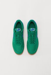 Zapatillas verdes de Nike con parte superior de lona, acentos azules, punta redonda y suela de goma natural. Los cordones están enhebrados a través de siete pares de ojales.