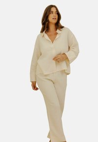Ensemble de vêtements d'intérieur beige clair comprenant une chemise boutonnée à coupe décontractée et manches longues, associée à un pantalon à jambe droite assorti. Tissu texturé.