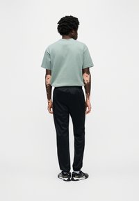 Πράσινο βαμβακερό μπλουζάκι, λαιμόκοψη με γιακά, κοντά μανίκια·  μαύρο στενό φούτερ παντελόνι· μαύρα αθλητικά παπούτσια. Όψη από πίσω. Λεία υφή, άνετη εφαρμογή.