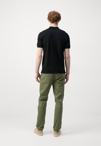 Camisa polo negra de manga corta, combinada con pantalones verde oliva. Ambas prendas tienen un corte casual y una textura de tela suave.
