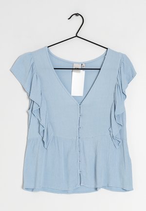 Blusa azzurro chiaro con scollatura a V, maniche corte arricciate e chiusura con bottoni. Realizzata in tessuto testurizzato, appesa a un gancio nero.