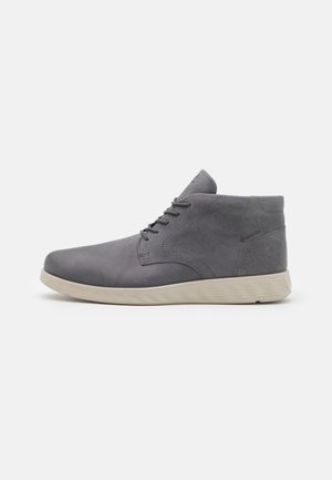 Botas de tobillo de cuero gris con una textura suave, punta redonda y cordones en la parte delantera. Presentan una suela ligera de color crema y un detalle de marca sutil.