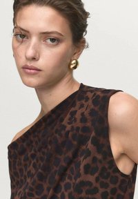 Brown leopard print blouse with an asymmetric design, featuring a single shoulder strap, lightweight fabric, and smooth texture. Gold hoop earrings.