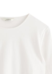 Vit kortärmad t-shirt med rundad halsringning, tillverkad av mjukt bomullsmaterial, med en etikett som visar varumärke och storleksinformation.