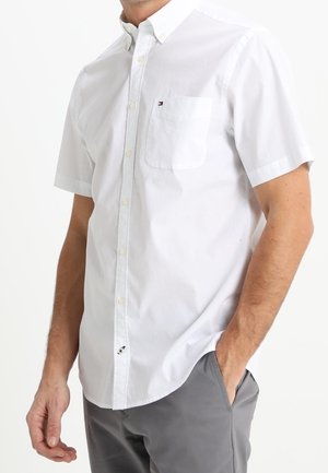 Koszula z krótkim rękawem, z kołnierzykiem, w białym kolorze, wykonana z bawełnianej tkaniny, z jedną kieszenią na piersi z małym logo i zapięciem na guziki.