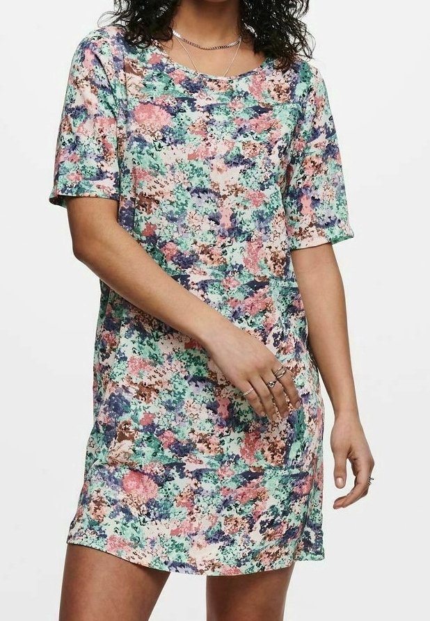 Personne portant une robe courte aux genoux à manches courtes avec un motif floral abstrait rose, vert, bleu et marron, avec des bagues aux doigts.