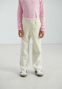 Pantalon en polaire blanche à coupe décontractée, taille élastique, associé à un haut à manches longues rose clair. Les baskets présentent un design blanc et marron.