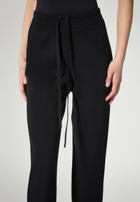 Sorte joggerbukser med snor i taljen, der har en glat tekstur og ribbet linning. Figurformet, tilspidset design.