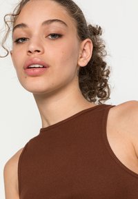 Top de alças castanho, com uma gola alta e design sem mangas. O material parece suave, com uma textura subtil e costuras bem acabadas nas bordas.