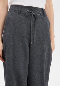 Dark gray trousers made of soft fabric, featuring a button closure and a front drawstring with metal tips. Smooth texture, relaxed fit.