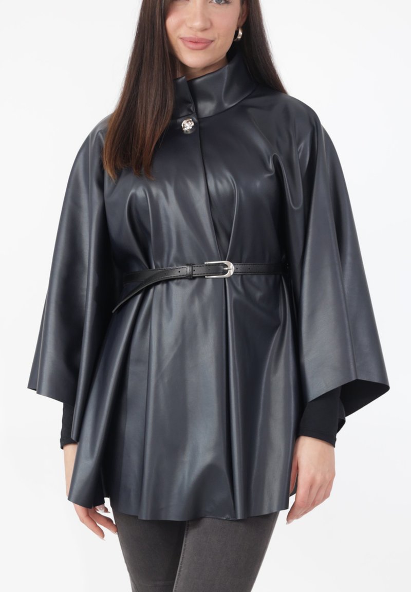 Sort kappe i kunstlæder med høj krave, knaplukning foran og indsnøret talje. Har brede ærmer og glat, skinnende tekstur.