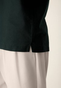 Haut en coton noir avec fentes latérales, associé à un pantalon en tissu beige clair. Mise en avant des couleurs et textures contrastées des deux vêtements.