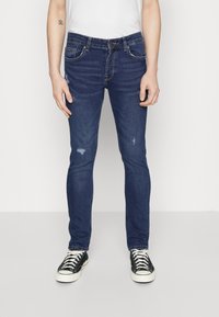 Jeans ajustados de denim azul oscuro con un ligero desgaste en los muslos, que presentan un diseño clásico de cinco bolsillos y cierre de cremallera.
