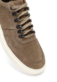 Zapatilla alta de cuero marrón con acabado texturizado, equipada con herrajes de cierre negro y cordones beige, suela de goma blanca.
