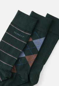 Three pairs of green socks: one with horizontal stripes in brown and cream, one with a diamond pattern in blue and brown, ribbed texture.