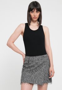 Zwarte geribde tanktop gecombineerd met een grijze houndstooth mini-jurk met een franjerand. De outfit toont een getailleerd silhouet en een gestructureerde stof.