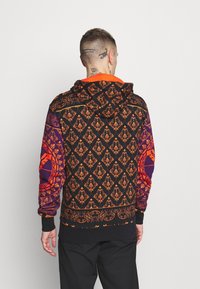 Felpa con cappuccio nera con vivaci motivi arancioni e viola, caratterizzata da disegni intricati, polsini a contrasto e un collo arancione.