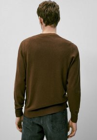 Maglione lavorato a maglia marrone con maniche lunghe, colletto rotondo, polsini a coste e una vestibilità morbida, abbinato a jeans scuri, visto da dietro.