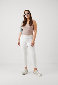 Top sin mangas a rayas con líneas naranjas y azules, jeans ajustados blancos y zapatillas deportivas plateadas. Los accesorios incluyen gafas de sol blancas y un bolso azul claro.