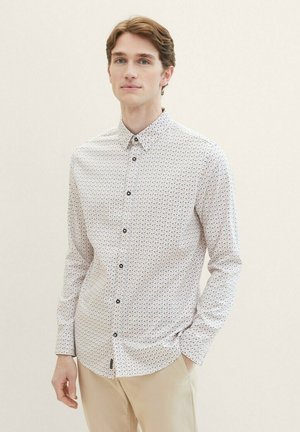 Witte blouse met lange mouwen en een geometrisch patroon in blauw, rood en geel. Voorzien van een knoopsluiting bij de kraag en zwarte knopen.