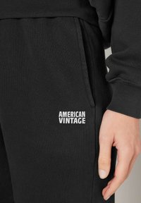 Svarta bomullsjoggers med ribbad midja och muddar. "AMERICAN VINTAGE"-logotyp i vitt på underbenet. Mjuk textur och avslappnad passform.