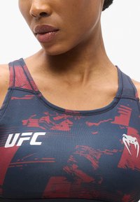 Brassière de sport bleue et rouge avec motif graphique, dotée d'un col rond et de bretelles étroites. Logo affiché sur le côté gauche.