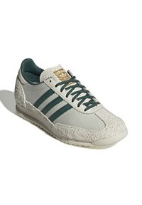 Ljusgrå sneaker med gröna ränder, vita texturerade detaljer, övre del i läder och en guldfärgad logotyp på tungan. Gummisulor.