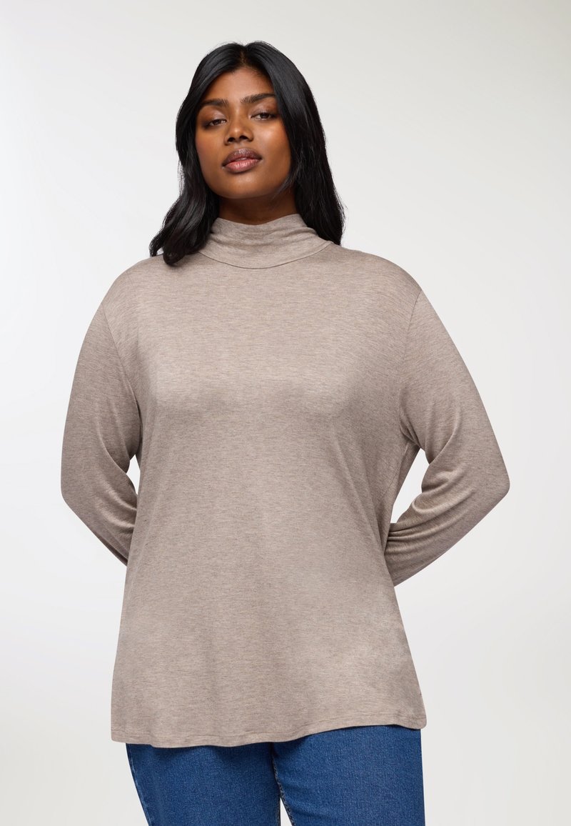 Beżowy oversize turtleneck z długim rękawem, wykonany z miękkiego materiału, z delikatnym połyskiem. W zestawieniu z niebieskimi dżinsami.