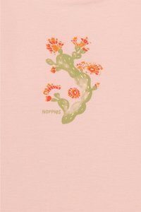Lichtroze T-shirt met een groene plantontwerp met oranje en rode bloemen, en het woord "NOPPIES" in het groen. Zachte, katoenen stof.