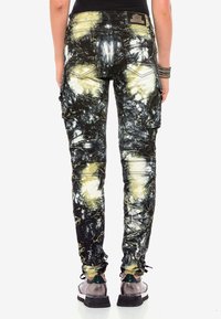 Pantalones cargo en un patrón de tie-dye negro y amarillo, con múltiples bolsillos, ajuste slim y un acabado de tela texturizada.