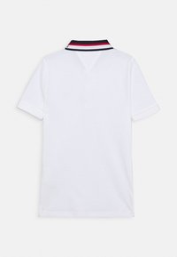 Valkoinen polo-paita, jossa on erottuva musta, punainen ja valkoinen raidallinen kaulus. Lyhyet hihat ja suora helma, valmistettu pehmeästä puuvillakankaasta.