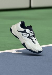 Fehér és tengerészkék sportcipő texturált felsőrésszel, párnázott szegéllyel, mintás talppal, az oldalán az EA7 logóval.