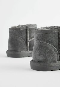 Graue Wildleder-Ankle-Boots mit einem weichen Innenfutter, abgerundetem Schaft und strukturierten Gummisohlen. Verstärkte Nähte und Stickdetails sind sichtbar.