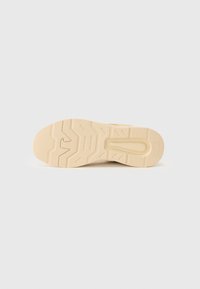 Beige sneakersåle med en teksturert gummioverflate, som har et sikksakkmønster og en sentral spor for fleksibilitet. Logoen er preget nær hælen.