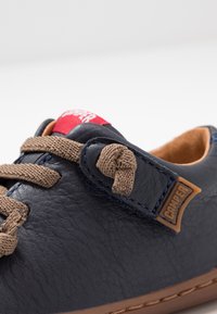 Scarpe in pelle blu navy con dettagli color nocciola, punta tonda e lacci marroni annodati. Presentano un'etichetta rossa e una superficie testurizzata.