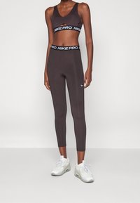 Braunes athletisches Crop Top mit Ausschnitt, kombiniert mit passenden figurbetonten Leggings mit einem schwarzen Nike Pro Bund und kleinem Logo.