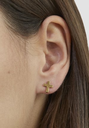Goldenes Kreuz-Stecker-Ohrring mit minimalistischem Design und glatter Oberfläche. Nahaufnahme eines durchbohrten Ohrs.