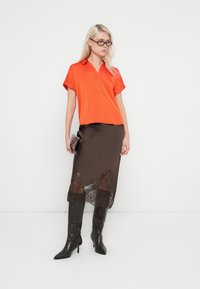 Short-sleeve orange blouse with a collar; paired with a brown satin skirt featuring lace detailing at the hem. Black knee-high stiletto boots.