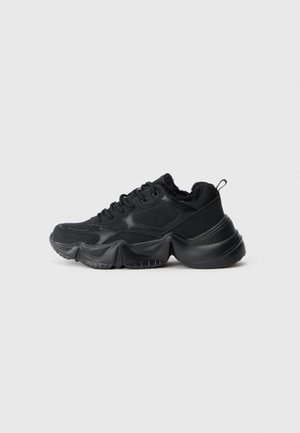 Schwarze Sneakers mit einer Mischung aus glatten und strukturierten Materialien, dicken Sohlen, runder Form und dekorativem Nähen. Sie verfügen über einen weichen, gepolsterten Kragen.