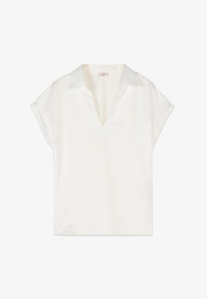 Bílá krátká halenka s výstřihem do V a volným střihem, vystavená na rovném povrchu bílé barvy.