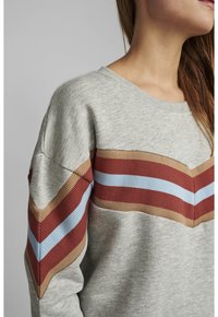 Sweat-shirt gris doté de rayures chevrons côtelées en rouge, bleu et beige sur la poitrine et les manches. Tissu doux et texturé.