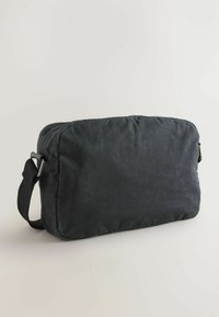 Sort canvas taske med rektangulær form, der har lynlåslukning, justerbar rem og kontrasterende tekstur i et slidstærkt materiale.