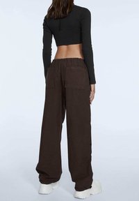 Bruine wijde broek met een elastische tailleband en twee achterzakken, gecombineerd met een zwart langemouwen crop top.