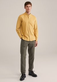 Cămașă galbenă cu mâneci lungi, cu guler chinezesc, asortată cu pantaloni verzi măslinii și pantofi negri de birou. Material neted și croială adaptată.