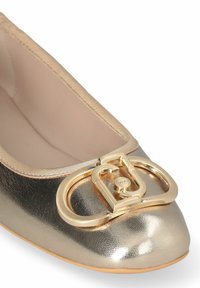 Ballet flat metallizzata oro con punta arrotondata, caratterizzata da una tomaia testurizzata, bordo a contrasto e un'ampia fibbia dorata ben evidente sulla parte anteriore.