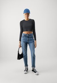Musthave mustre bodo pimedas pikka varrukatega cropped särk, helesinised kõrge vöökoha teksad, mustad kingad valgete talladega, hoiab väikest musta käekotti, teksahat. 