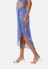 Blue patterned midi skirt with a high slit, made of lightweight fabric. Paired with white strappy heels, featuring a low square heel.