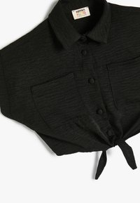 Camisa de niños negra, de manga corta, con cuello, tejido texturizado, cierre frontal de botones, dos bolsillos en el pecho y detalle de dobladillo atado.