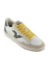 Zapatilla blanca con detalles en verde, detalles de ante beige y cordones amarillos. Presenta una puntera perforada y una suela de goma texturizada. La etiqueta dice "Victoria 1985."