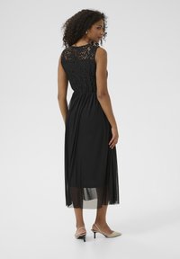Black dress featuring a lace bodice, knee-length sheer skirt, and defined waist. Paired with pointed-toe heels. Smooth, glossy texture.